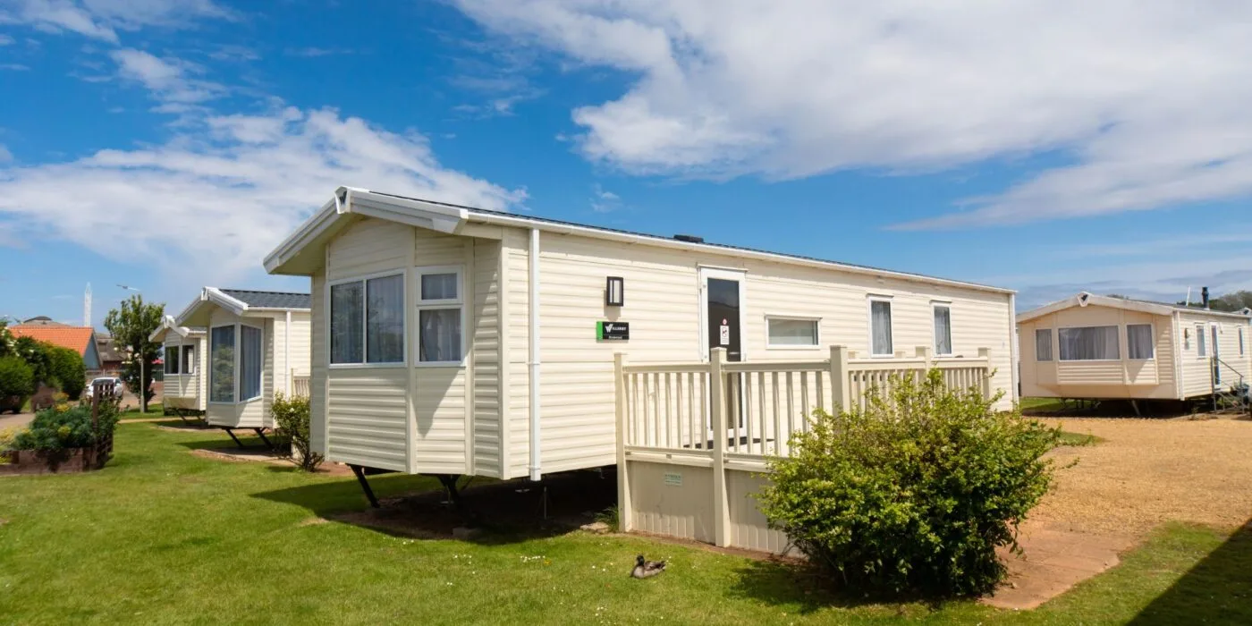 Cream coloured modern static caravan with a veranda and bright blue sky sprinkled with clouds.
